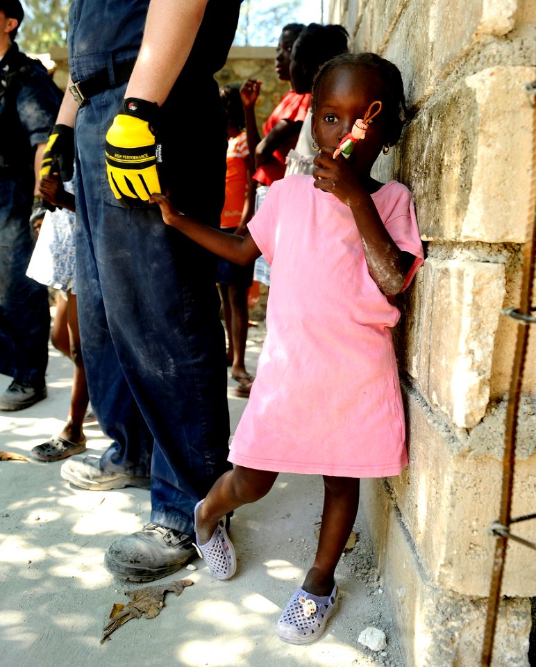 US Navy 100129-N-5345W-279 A young Haitian girl holds onto a Sailor from the multi-purpose amphibious assault ship USS Bataan (LHD 5) while watching other Bataan Sailors clear rubble and debris