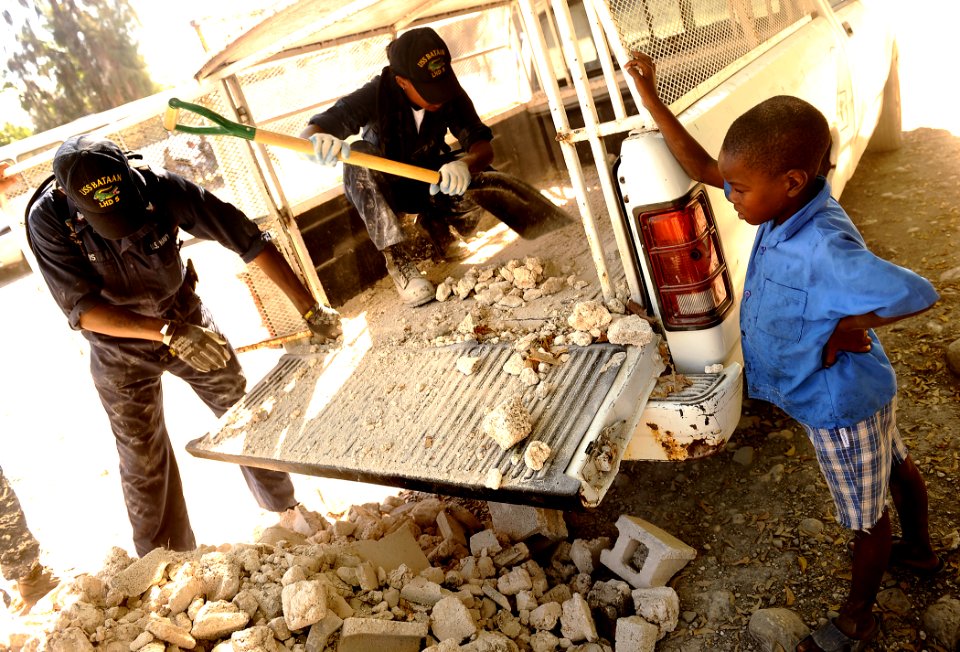 US Navy 100129-N-5345W-184 A young Haitian boy watches as Sailors from the multi-purpose amphibious assault ship USS Bataan (LHD 5) clear a load of rubble from the bed of a truck