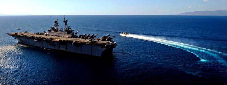 US Navy 100128-N-5345W-308 An MH-60S Sea Hawk helicopter lifts off from the flight deck of the multi-purpose amphibious assault ship USS Bataan (LHD 5) as a landing craft air cushion (LCAC)