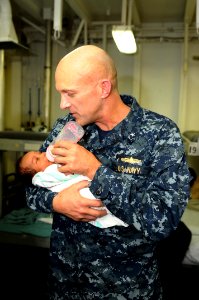 US Navy 100130-N-8936G-028 Rear Adm. David Thomas Jr., commander of Carrier Strike Group 2, feeds a Haitian infant in the medical department of the amphibious assault ship USS Nassau (LHA 4)