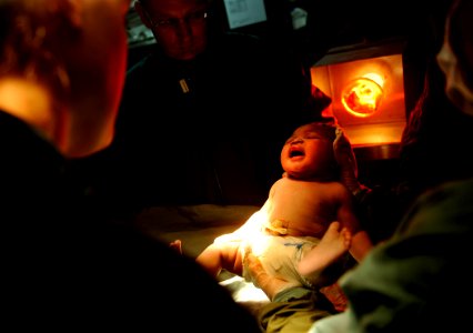 US Navy 100130-N-5345W-031 Medical personnel aboard the multi-purpose amphibious assault ship USS Bataan (LHD 5) hold a newborn baby boy under a heat lamp photo