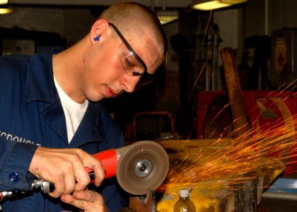 US Navy 100202-N-2000D-071 Hull Technician Fireman Dustin McDougle grinds a part from the stern gate box during repairs aboard the amphibious dock landing ship USS Carter Hall (LSD 50)