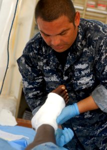 US Navy 100203-N-2000D-295 Hospital Corpsman 2nd Class Sergio Hernandez, assigned to the amphibious dock landing ship USS Carter Hall (LSD 50), treats the foot wound of a Haitian woman at the Hospital Cardinal de Legar in Leog