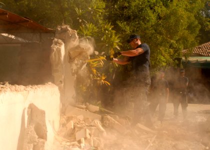 US Navy 100203-N-2000D-045 Electrician's Mate 2nd Class Travis Turnipseed, assigned to the amphibious dock landing ship USS Carter Hall (LSD 50), uses a sledge hammer to knock down the wall of a dilapidated building at the Hosp
