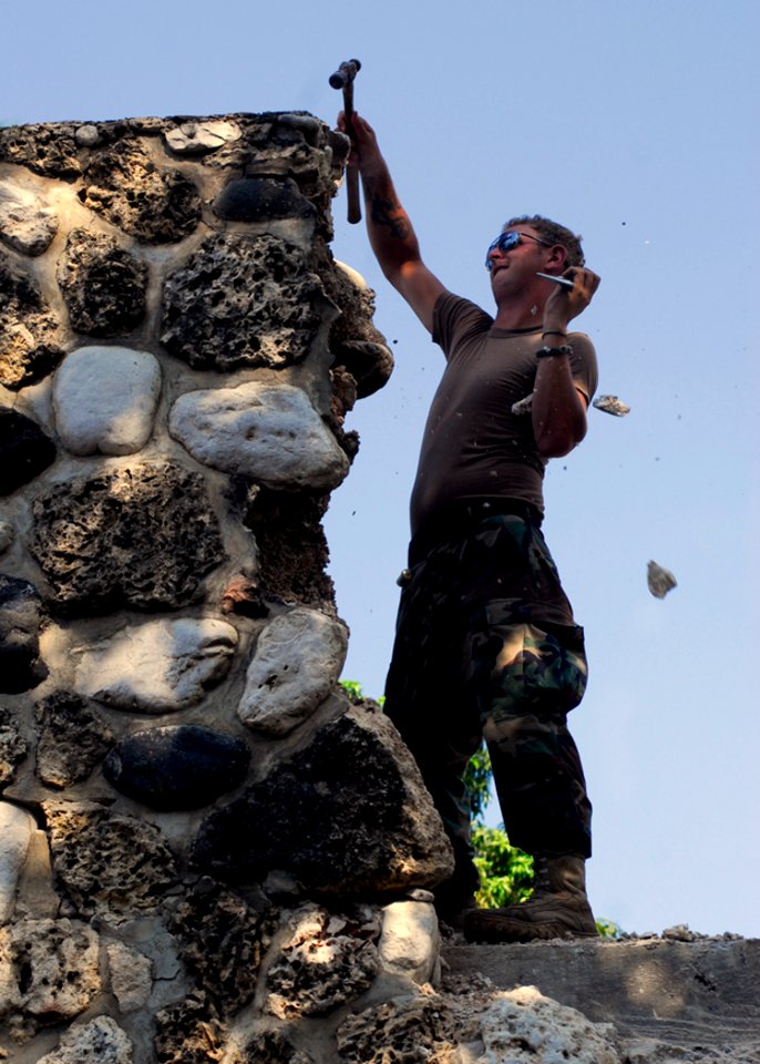US Navy 100205-N-5244H-016 tilitiesman 3rd Class John Pruitt chips away the damage on a building at Hospital Cardinal Leger