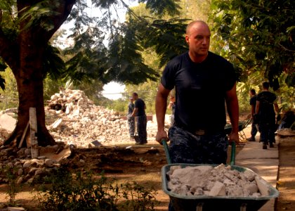 US Navy 100206-N-2000D-091 Seaman Eric Shields, from Indianapolis, Ind., assigned to the amphibious dock landing ship USS Carter Hall (LSD 50), rolls a wheelbarrow filled with rubble from a destroyed building at the Hospital Ca