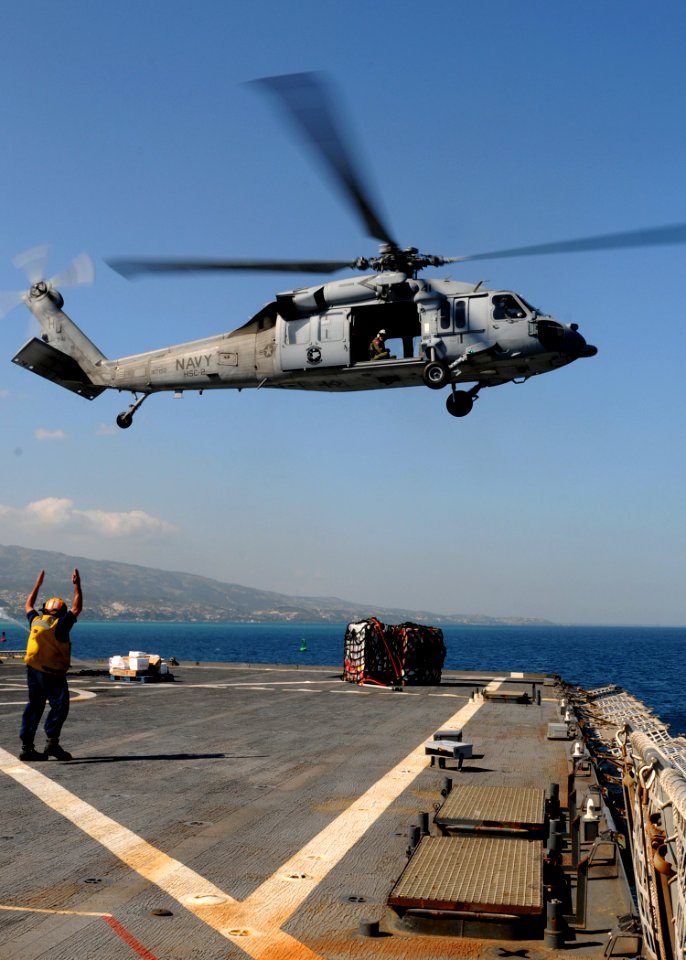 US Navy 100204-N-6676S-009 A Sailor directs an MH-60S Sea Hawk helicopter away from the flight deck of the amphibious dock landing ship USS Gunston Hall (LSD 44) during a vertical replenishment