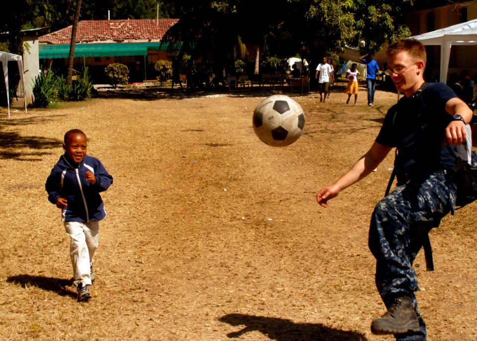 US Navy 100206-N-2000D-318 Hospital Corpsman 3rd Class Kelby Mays, from Weatherford, Texas, assigned to the amphibious dock landing ship USS Carter Hall (LSD 50), plays soccer with a boy at a field treatment camp at the Hospita