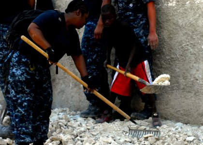 US Navy 100209-N-5244H-044 A Haitian boy helps Information Systems Technician 2nd Class Shaunte Stafford remove rubble photo
