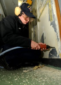 US Navy 100217-N-6233H-026 Operations Specialist 3rd Class Eric Martin uses a needle gun to remove old paint on a bulkhead aboard the aircraft carrier USS George Washington (CVN 73)