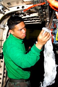 US Navy 100222-N-3327M-029 Aviation Machinist's Mate 2nd Class Raynard Eugenio, assigned to the Warhawks of Strike Fighter Squadron (VFA) 97, performs maintenance on the engine of an F-A-18C Hornet aboard the aircraft carrier U
