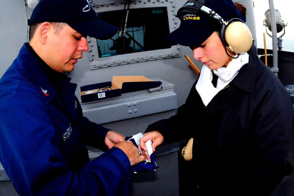 US Navy 100222-N-7939W-196 Quarter Master 2nd Class Ramon Sturdivant teaches Quarter Master Seaman Andrea Martinez how to fold a flag aboard the aircraft carrier USS Nimitz (CVN 68)