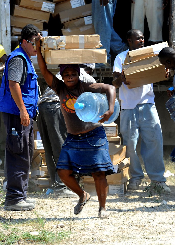 US Navy 100224-N-5961C-008 A Haitian woman carries a five gallon jug of water and two pieces of plastic sheeting