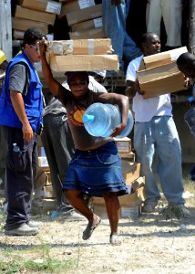 US Navy 100224-N-5961C-008 A Haitian woman carries a five gallon jug of water and two pieces of plastic sheeting