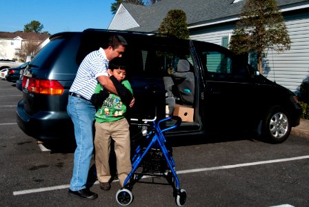 US Navy 100306-N-5319A-003 Lt. Cmdr. Santiago Camano assists his ten-year-old son Joseph to his walker during a routine therapy visit at the Diane Epplein ^ Assoc. Pediatric Therapy facility