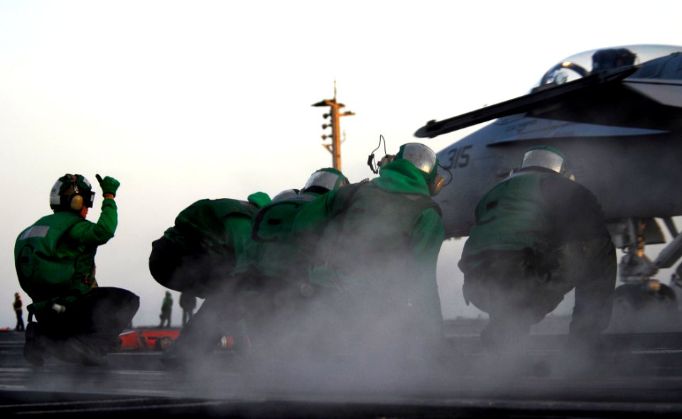US Navy 100319-N-6538W-432 Aviation Boatswain's Mates (Equipment) crouch down as an F-A-18C Hornet from the Raiders of Strike Fighter Squadron (VFA) 125 launches from the Nimitz-class aircraft carrier USS John C. Stennis (CVN 7