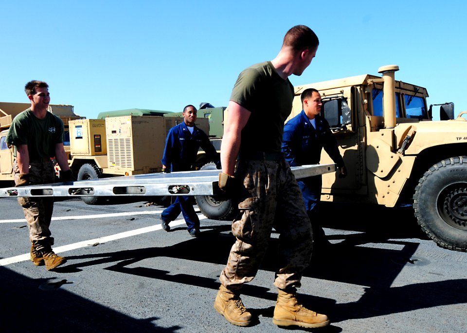 US Navy 100328-N-7948R-333 Sailors and Marines carry parts of a personnel transport module prior to assembly aboard the amphibious dock landing ship USS Pearl Harbor (LSD 52)