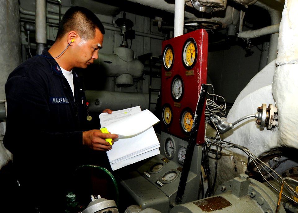 US Navy 100417-N-7948R-034 Machinist's Mate 3rd Class Ferdinand Macapagal checks the gauges of a forced draft blower in the forward main machinery room aboard the amphibious assault ship USS Peleliu (LHA 5)