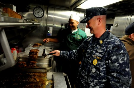 US Navy 100423-N-9818V-144 Master Chief Petty Officer of the Navy (MCPON) Rick West flips burgers with Culinary Specialist Seaman Mykal Martin aboard the Virginia-class attack submarine USS New Mexico (SSN 779)