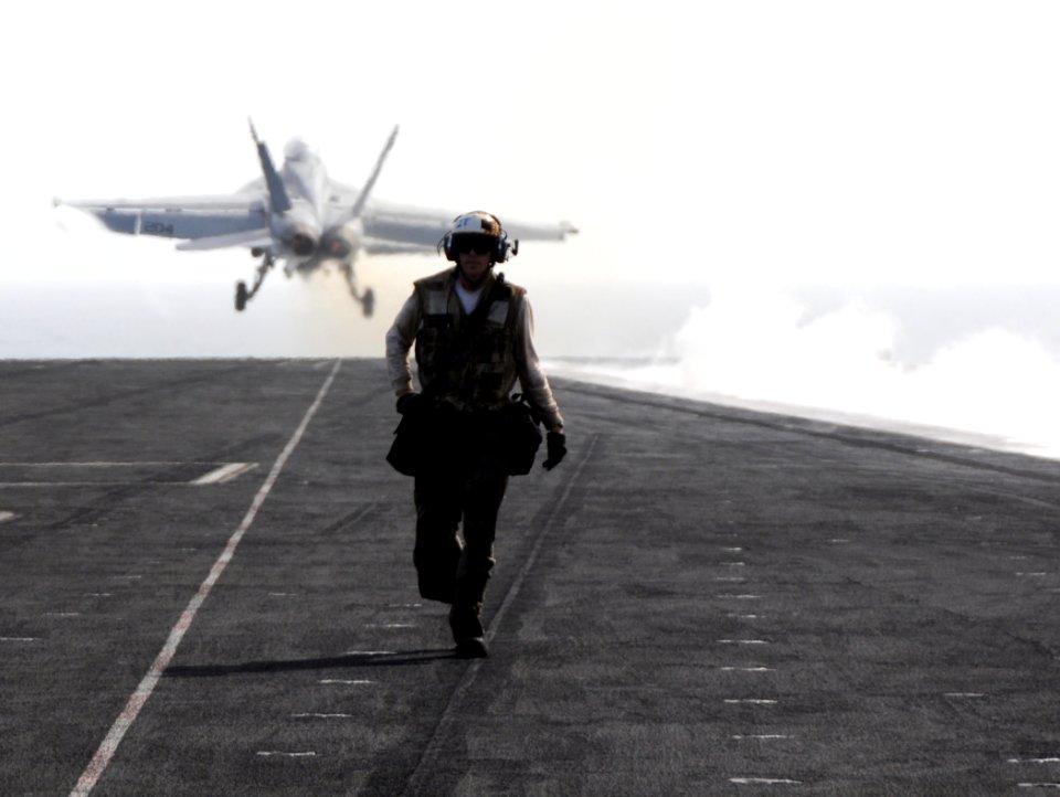 US Navy 100523-N-4236E-260 A Sailor walks along the flight deck as an F-A-18F Super Hornet assigned to the Jolly Rogers of strike fighter squadron (VFA) 103 launches from the aircraft carrier USS Dwight D. Eisenhower (CVN 69)