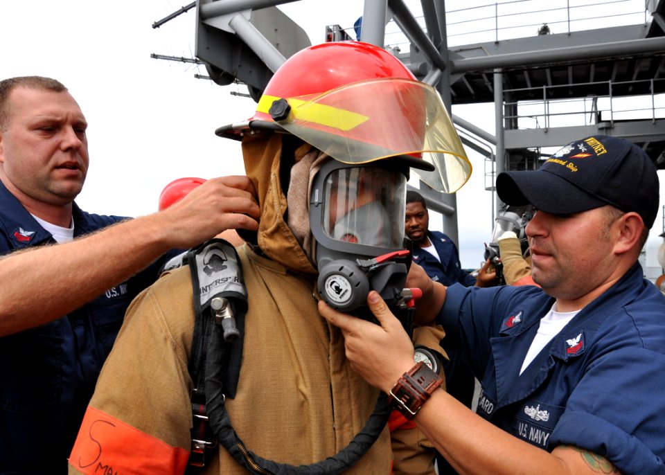 US Navy 100526-N-5483N-064 Navy Counselor 1st Class Robert Brock, left, assists Electronics Technician Seaman Jonathan Sanchez in donning firefighting gear while Fire Controlman 1st Class Scott Bouchard checks for a proper seal
