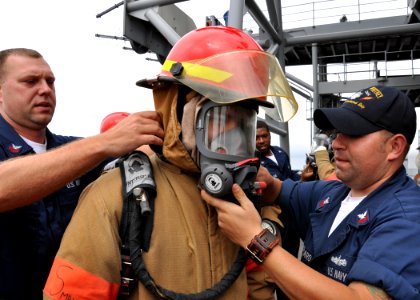 US Navy 100526-N-5483N-064 Navy Counselor 1st Class Robert Brock, left, assists Electronics Technician Seaman Jonathan Sanchez in donning firefighting gear while Fire Controlman 1st Class Scott Bouchard checks for a proper seal