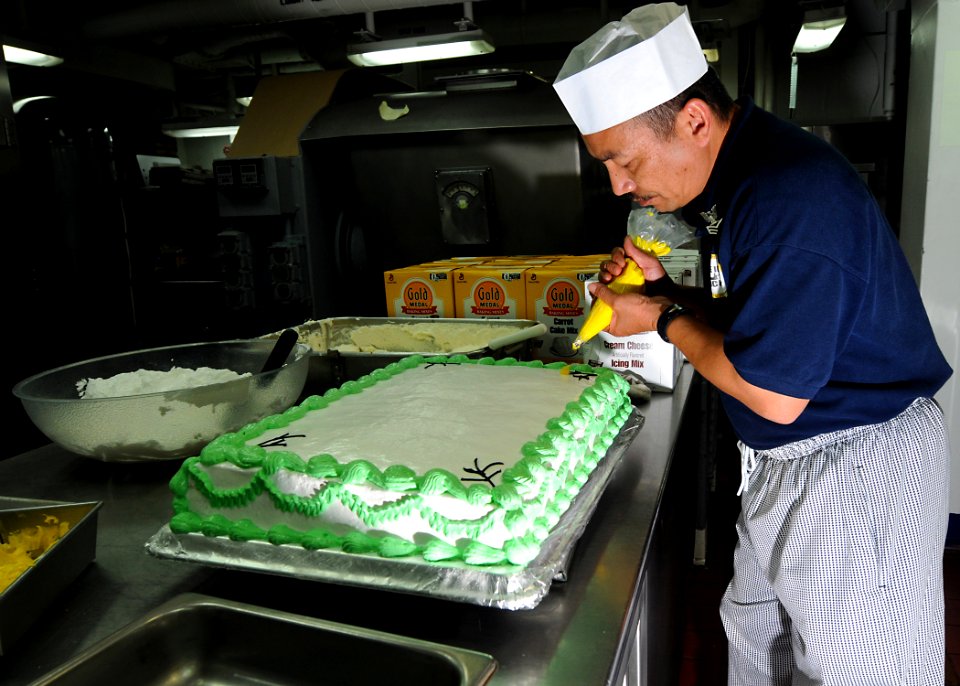 US Navy 100528-N-7949R-236 Culinary Specialist 1st Class Lamberto Vitug decorates a birthday cake for Sailors celebrating May birthdays aboard the amphibious assault ship USS Peleliu (LHA 5)
