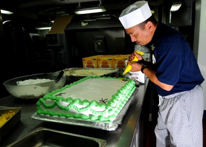 US Navy 100528-N-7949R-236 Culinary Specialist 1st Class Lamberto Vitug decorates a birthday cake for Sailors celebrating May birthdays aboard the amphibious assault ship USS Peleliu (LHA 5)