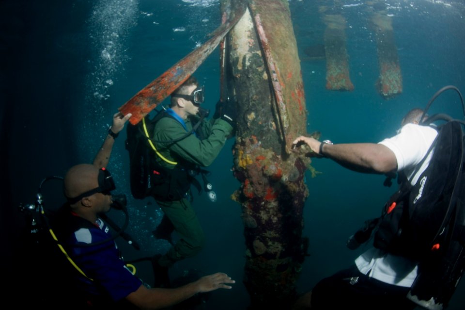 US Navy 100607-N-1134L-158 Hospital Corpsman 1st Class Michael Faasen, center, assigned to Mobile Diving and Salvage Unit (MDSU) 2, scrapes away marine growth and looks for structural damage during a pier inspection with Region