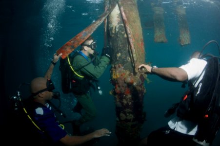 US Navy 100607-N-1134L-158 Hospital Corpsman 1st Class Michael Faasen, center, assigned to Mobile Diving and Salvage Unit (MDSU) 2, scrapes away marine growth and looks for structural damage during a pier inspection with Region