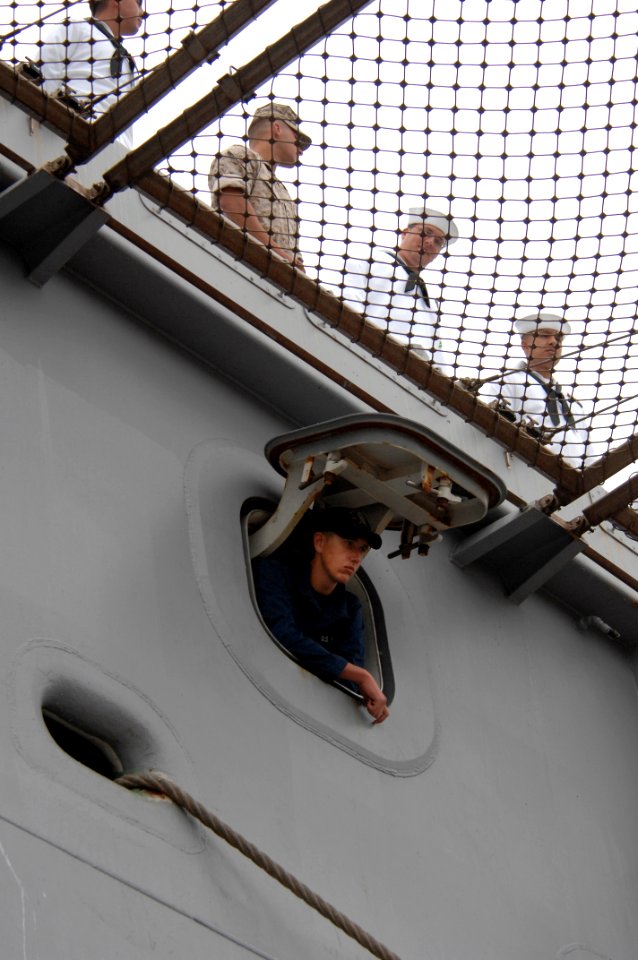 US Navy 100610-N-6477M-757 A line petty officer assigned to the amphibious transport dock ship USS New Orleans (LPD 18) looks out through the aft mooring station hatch while others man the rails as New Orleans departs from Nava