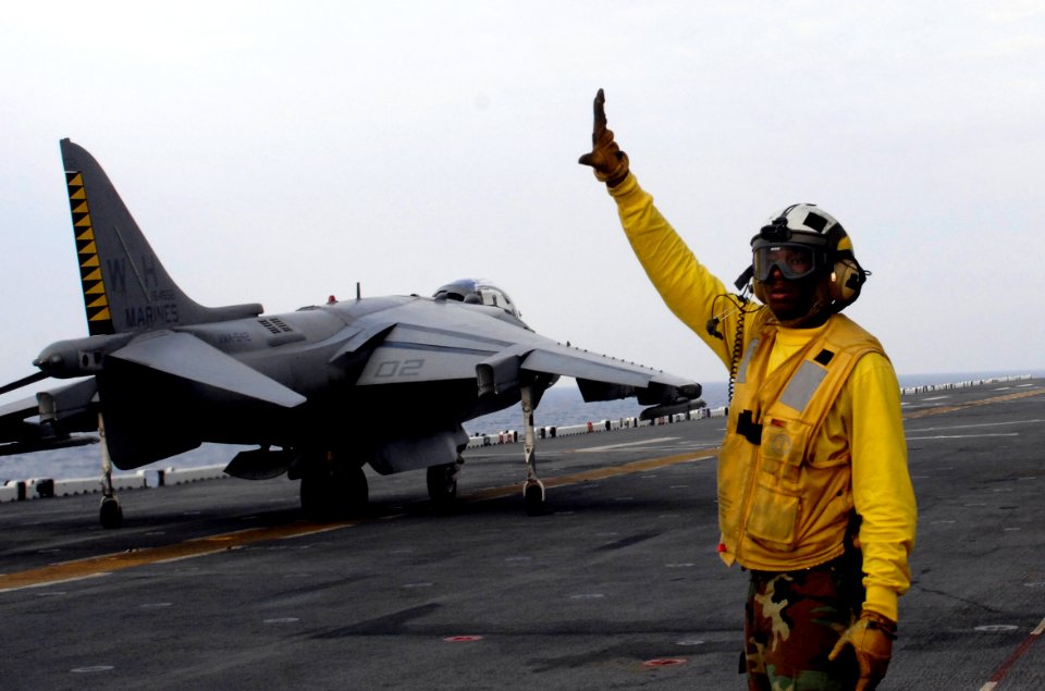US Navy 100618-N-3852A-146 Aviation Boatswain's Mate (Handling) 3rd Class Joshua Jackson signals a Marine Corps AV-8B Harrier II during flight operations aboard the amphibious assault ship USS Wasp (LHD 1)