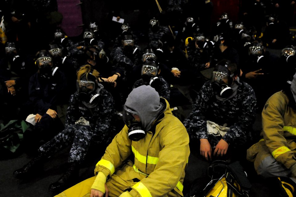 US Navy 100621-N-9132C-120 Sailors assigned to the aircraft carrier USS Ronald Reagan (CVN 76) sit in the hangar bay wearing gas masks during a general quarters exercise