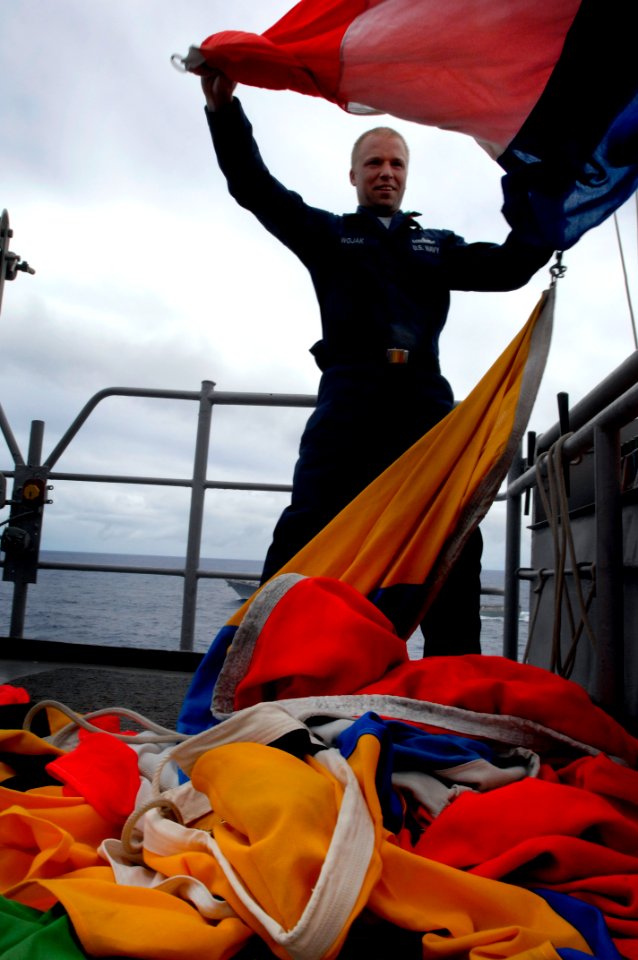 US Navy 100619-N-6477M-687 Quartermaster 3rd Class Cameron Wojak prepares to stow away signal flags after a flag hoist drill aboard USS Cleveland (LPD 7)