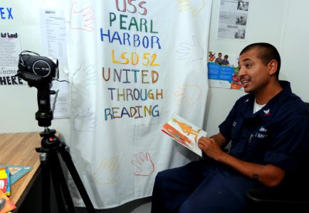 US Navy 100706-N-7948R-017 Quartermaster 2nd Class Abraham Velez, from Los Angeles, is videotaped reading a book to his children aboard the amphibious dock landing ship USS Pearl Harbor (LSD 52) photo