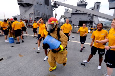 US Navy 100709-N-8335D-135 Sailors cheer for a teammate carrying an aqueous film forming foam (AFFF) can during a damage control Olympics firefighting ensemble relay on the flight deck of the amphibious dock landing ship USS Ha