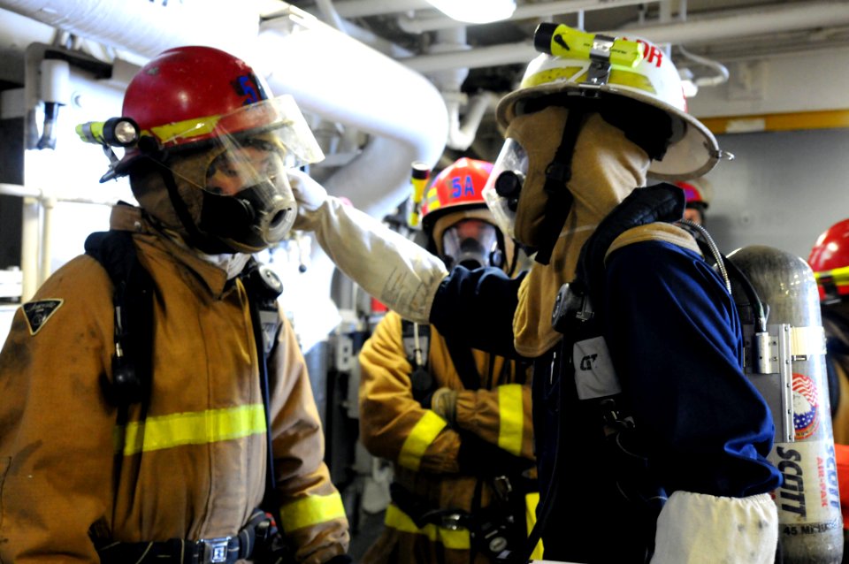 US Navy 100713-N-3852A-443 Damage Controlman 3rd Class Chad Noss, assigned scene leader for Damage Control Repair Locker 5A, assists his repair party team member adjust his helmet