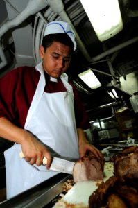 US Navy 100710-N-7191M-012 Culinary Specialist Seaman Apprentice Marco Valdez slices roast pork in the aft galley aboard USS George Washington (CVN 73)