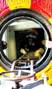 US Navy 100713-N-3852A-484 Seaman Cory Thomas, from Tallahassee, Fla., emerges from an emergency escape scuttle after setting smoke boundaries during a main space fire drill aboard the amphibious assault ship USS Wasp (LHD 1)