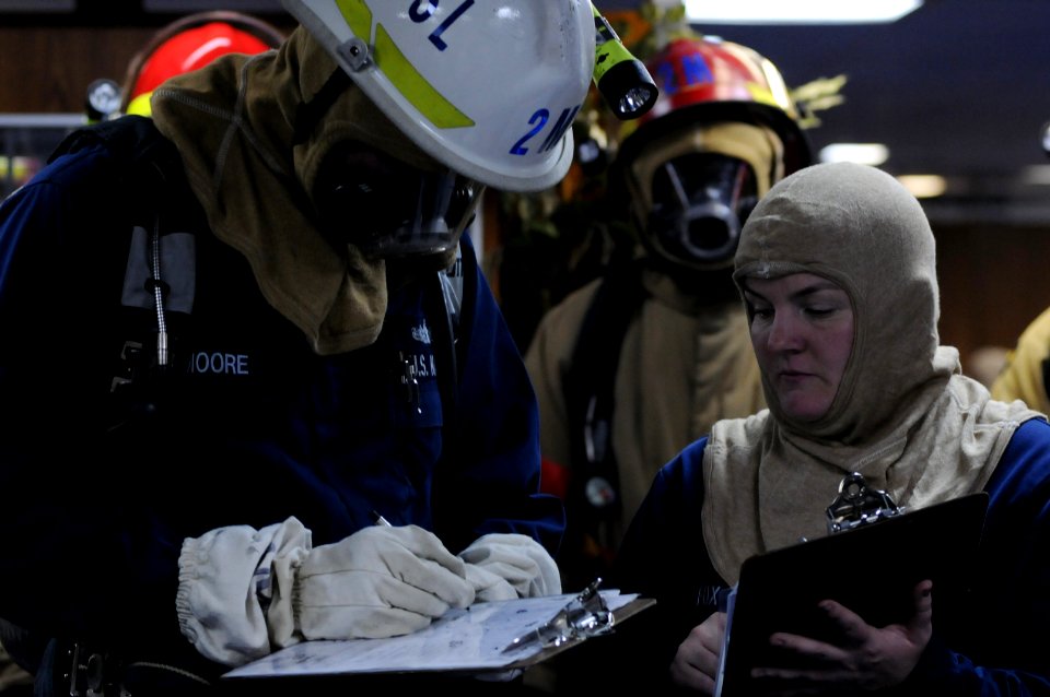 US Navy 100720-N-3852A-436 Damage Controlman 2nd Class Samuel Moore, left, passes information concerning the progress of a simulated casualty to Damage Controlman 1st Class Deidre Fox during a main space fire drill
