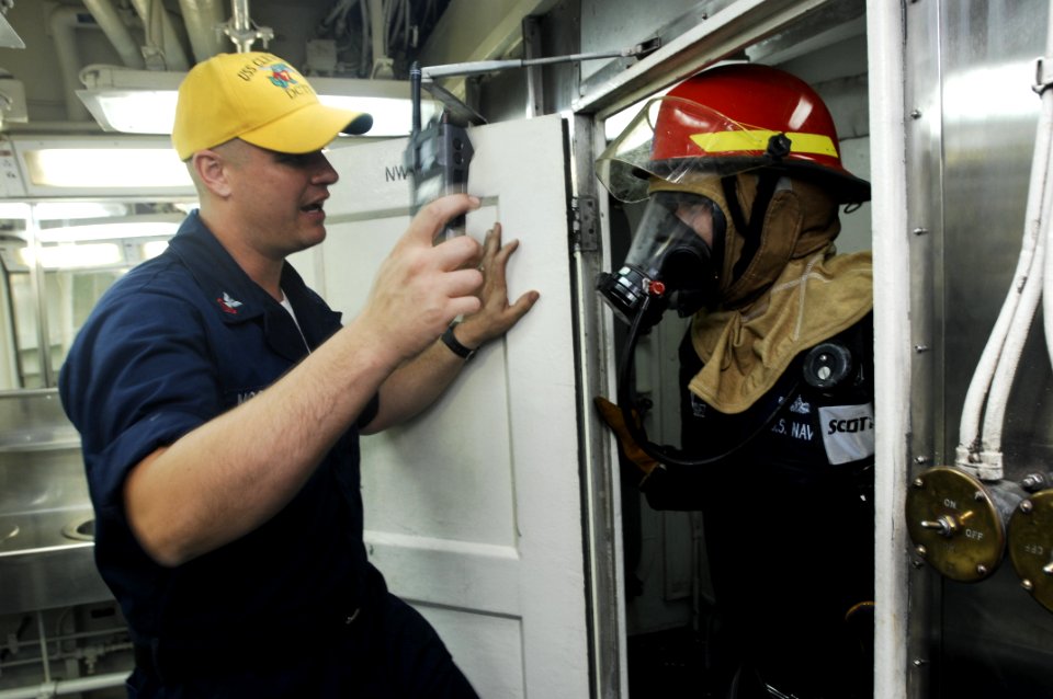 US Navy 100721-N-6477M-632 Damage Controlman 1st Class Joseph McGowan, a damage control training team member, advises Machinery Repairman 2nd Class Anthony Rodriguez during a fire drill