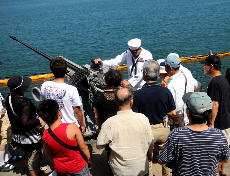 US Navy 100724-N-3283P-176 Fire Controlman 1st Class Casey Edgar explains the capabilities of the 25mm cannon aboard the guided-missile destroyer USS Russell (DDG 59) during an open ship tour