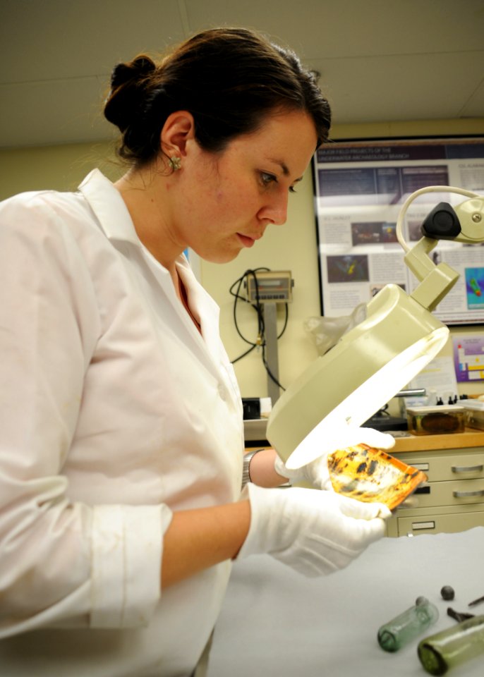 US Navy 100803-N-9671T-007 Kate Morrand, an artifact conservator at Naval History and Heritage Command, inspects a piece of pottery recovered from the wreck of the sloop-of-war USS Scorpion