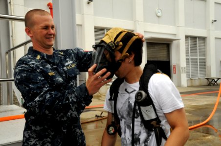 US Navy 100812-N-3283P-005 Chief Damage Controlman Matt Walz assists Yusuke Kawanabe with his fire fighting gear during a damage control demonstration at the Yokosuka Fire Fighting and Damage Control Training Facility