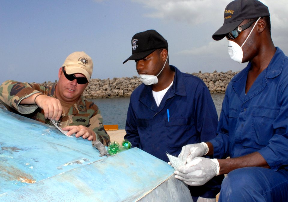 US Navy 100819-N-4971L-082 Equipment Operator 2nd Class Jeremy Hall demonstrates proper fiber glass repair techniques to members of the Barbados Defense Forces as they repair damage on a small boat during a subject matter exper