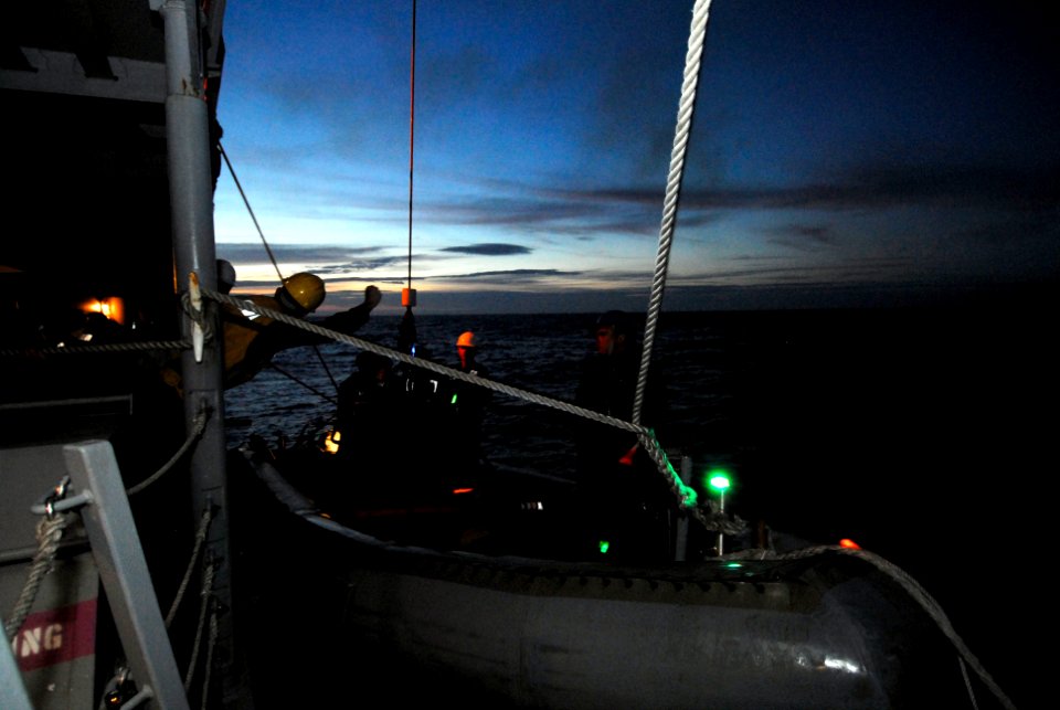US Navy 100821-N-7638K-189 Boatswain's Mate Seaman Daniel Waller signals as Sailors lower a rigid-hull inflatable boat during a night evolution of a man overboard drill