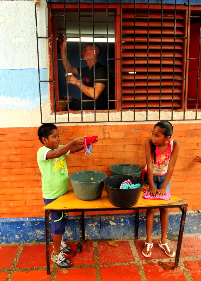 US Navy 100821-N-9301W-749 Lt. Lance Ruth, assigned to the guided-missile frigate USS Klakring (FFG 42), paints window shutters as children clean wiping rags during a joint community service project with the Colombian national