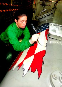 US Navy 100826-N-0569K-011 Aviation Boatswain's Mate (Equipment) Airman Meghan E. Gokey paints the American flag on a stowage tank in arresting gear engine room four