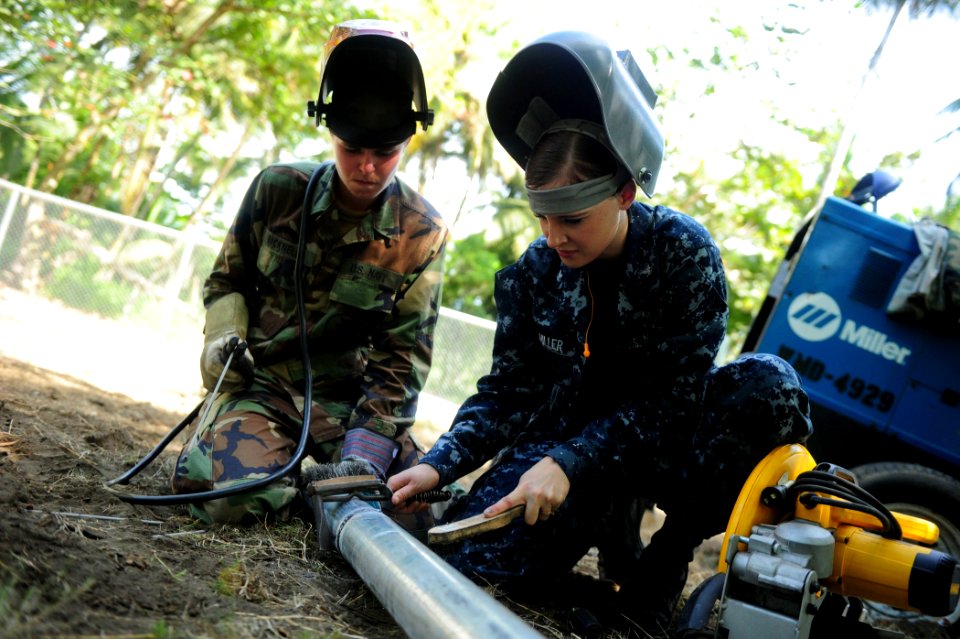 US Navy 100827-N-1531D-159 Steelworker Constructionman Lindzie Bicknell watches as Hull Maintenance Technician 3rd Class Yanina Schiller cleans up welding points from two fused galvanized pipes