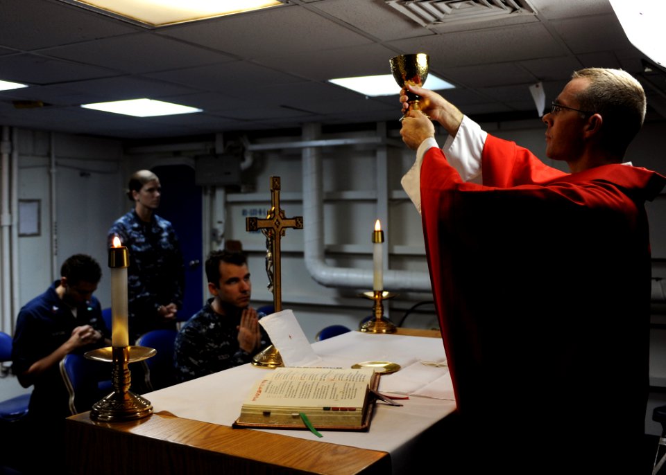 US Navy 100914-N-4973M-014 Lt. Benton Garrett raises the mass grail inside the chapel while Sailors pray during Catholic Mass